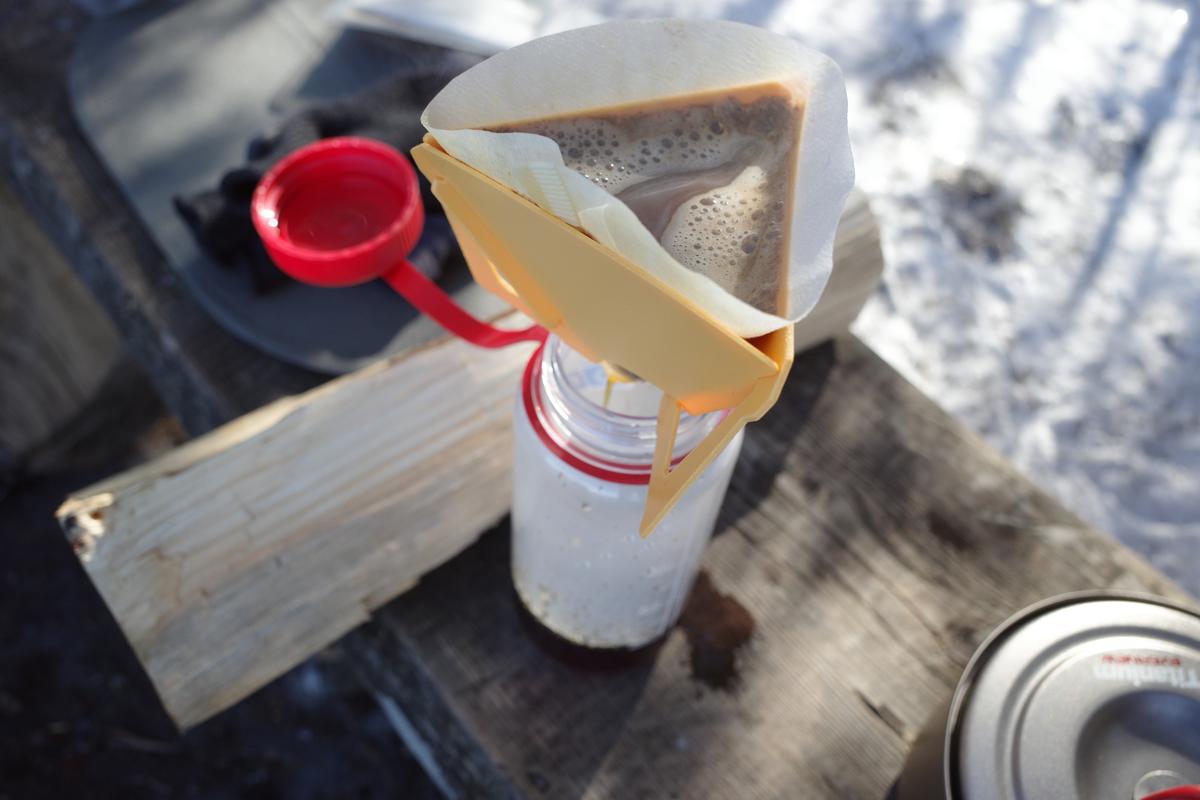 A coffee dripper on top of a Nalgene bottle on a bench outdoors.