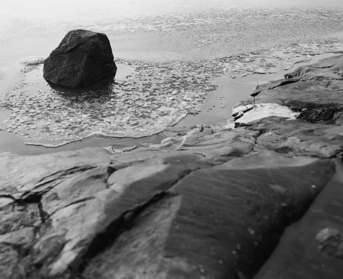 A rock in the sea, surrounded by a crust of thin ice.