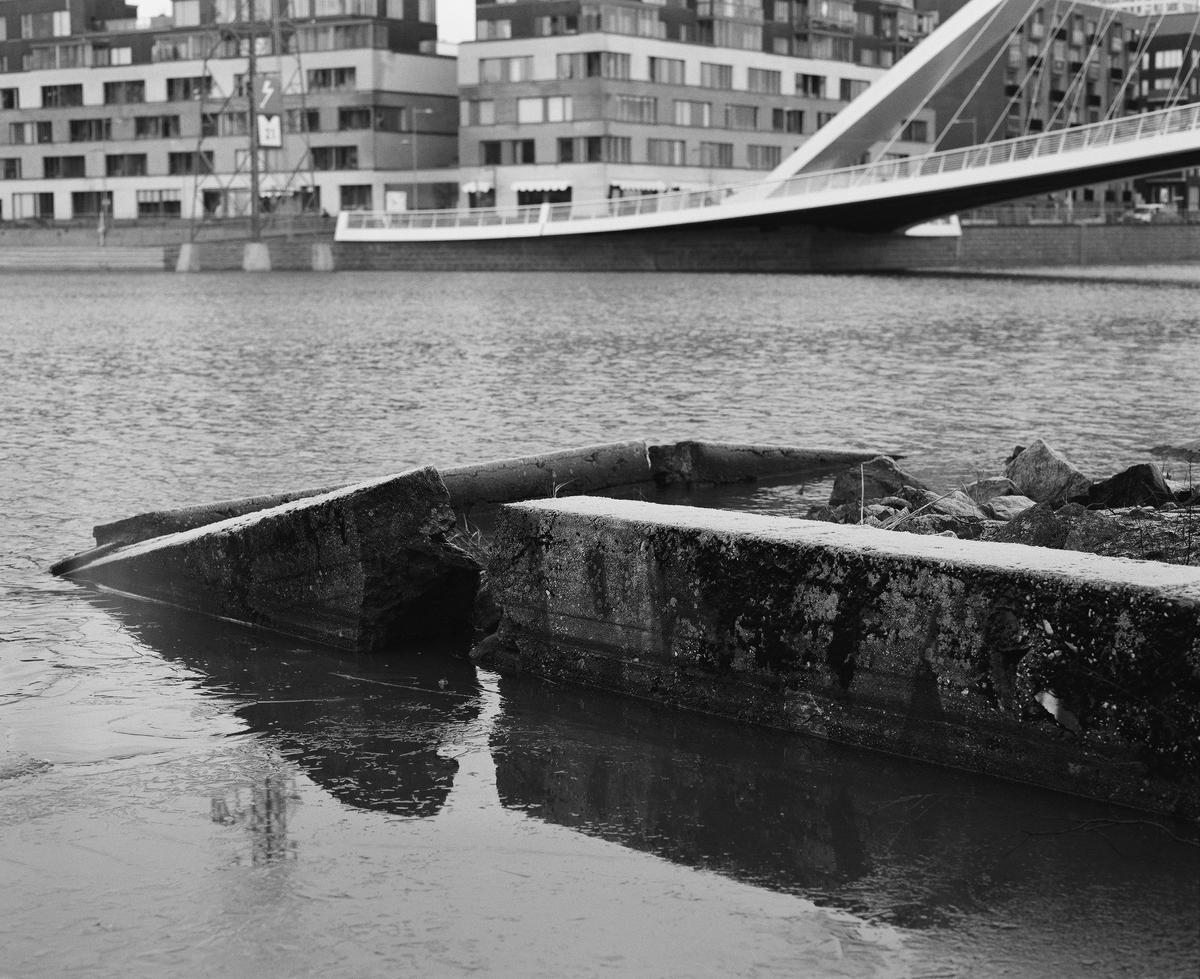 The remains of a pier in sea. There's a bridge in the background.