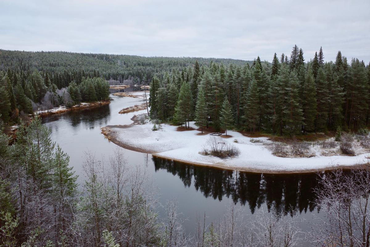 A curve of river in the middle of a forest. There's snow on the shore.