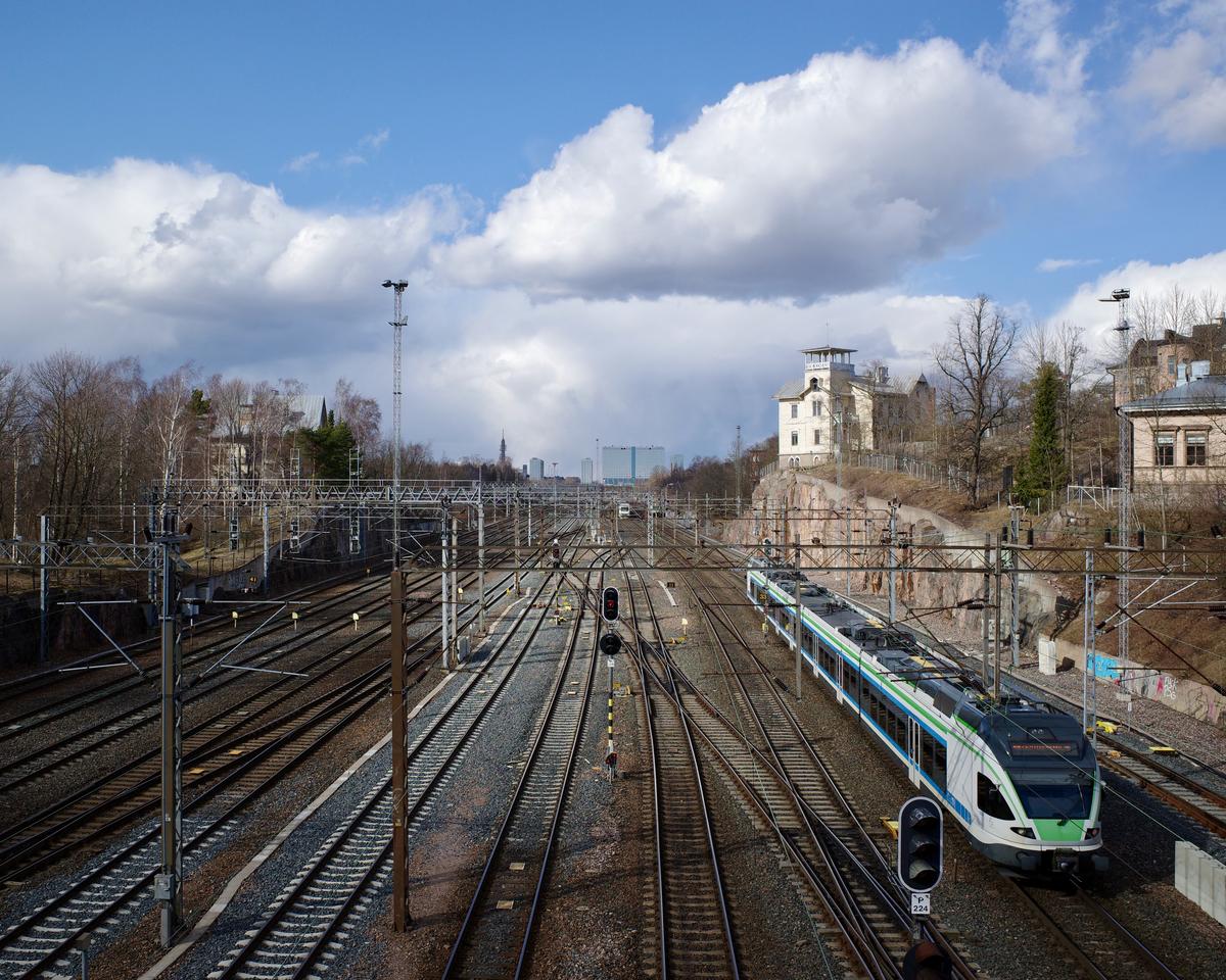 A train in a railyard. The Mall of Tripla shopping center can be seen in the background.